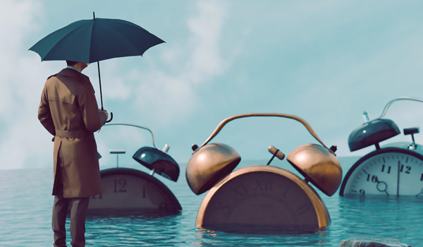 A person holding an umbella looking at giant alarm clocks that are floating in water