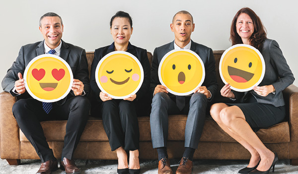 Four professional people sitting on a couch and holding emoji faces