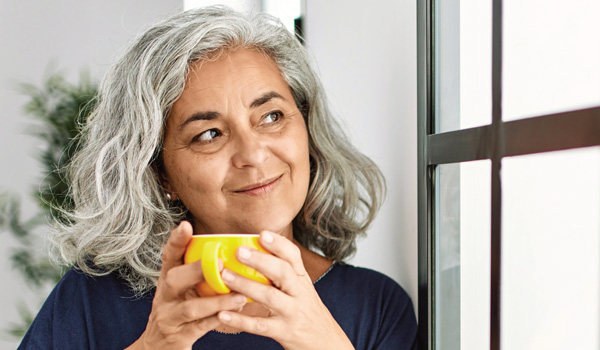 Older woman holding a cup and looking out a window